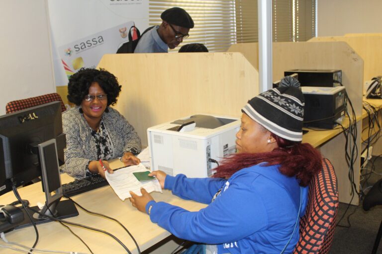 A woman filling out an SRD grant application form at a SASSA office counter, Apply for SASSA SRD Grant June 2025 Application