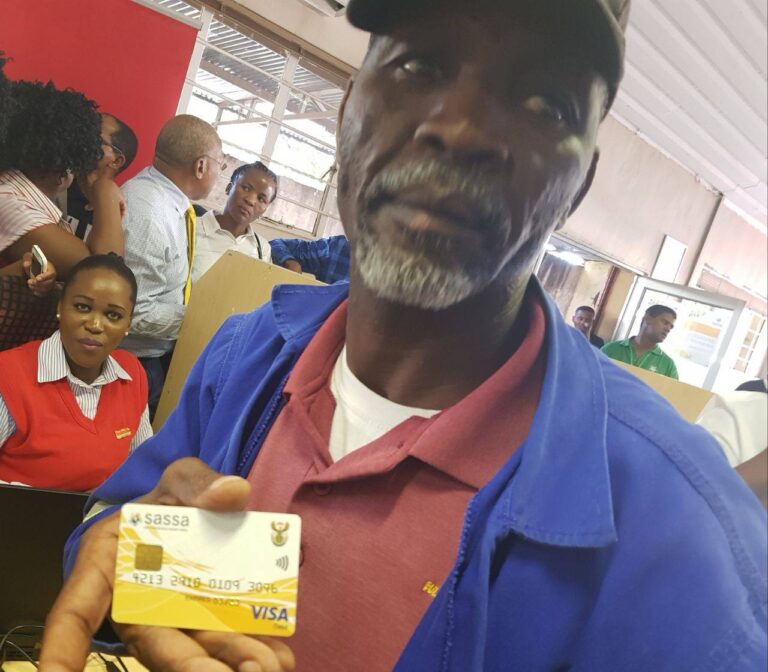 SASSA beneficiary holding Gold Card at Postbank for May 2025 grant withdrawal, SASSA Grant Payments Now Face Bank Charges